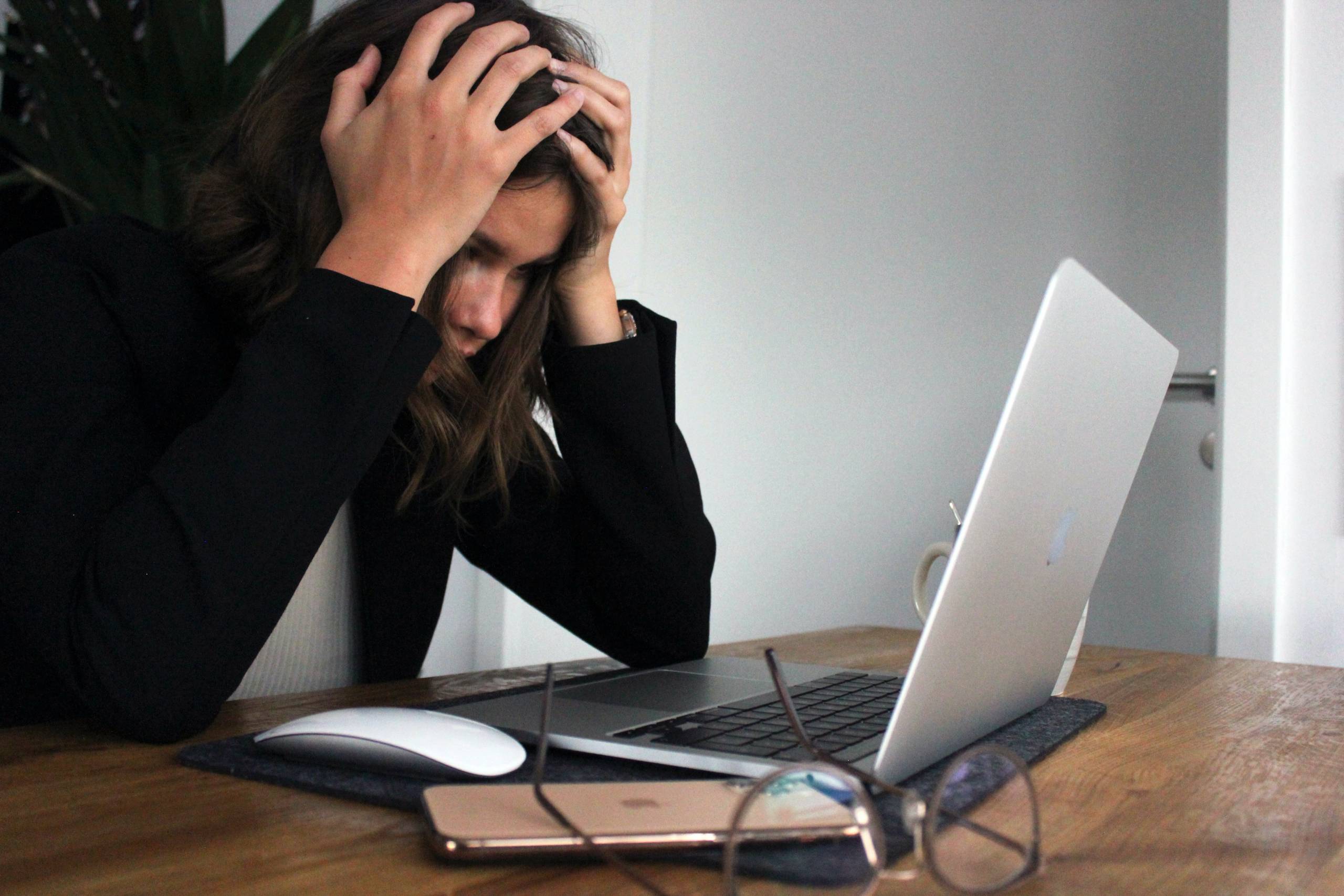 woman-at-desk-in-front-of-laptop-appears-stressed-holds-head-in-hands